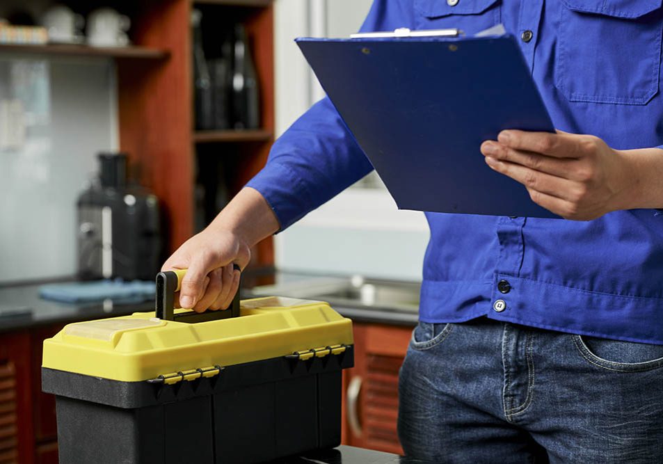 Close-up of repairman standing in uniform with toolbox and holding clipboard, he finished his work in domestic kitchen in apartment